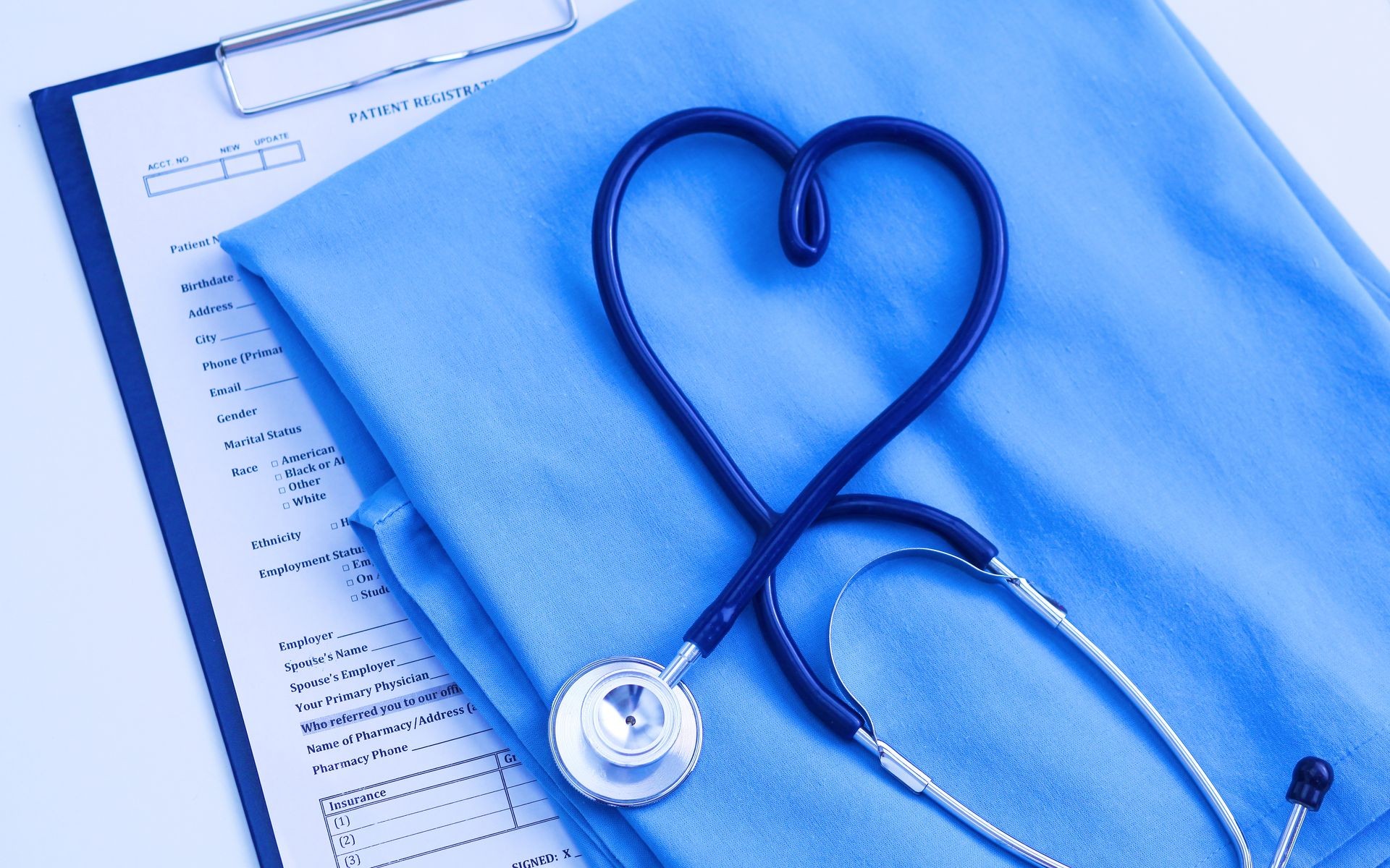 Medical stethoscope twisted in heart shape lying on patient medical history list and blue doctor uniform closeup.